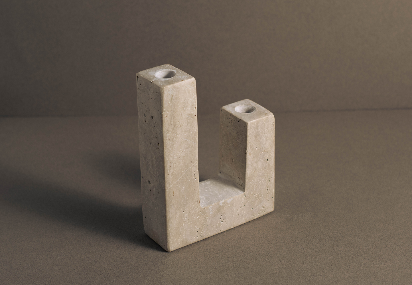 L-shaped candle holder in travertine with polished finish on a modern tabletop.