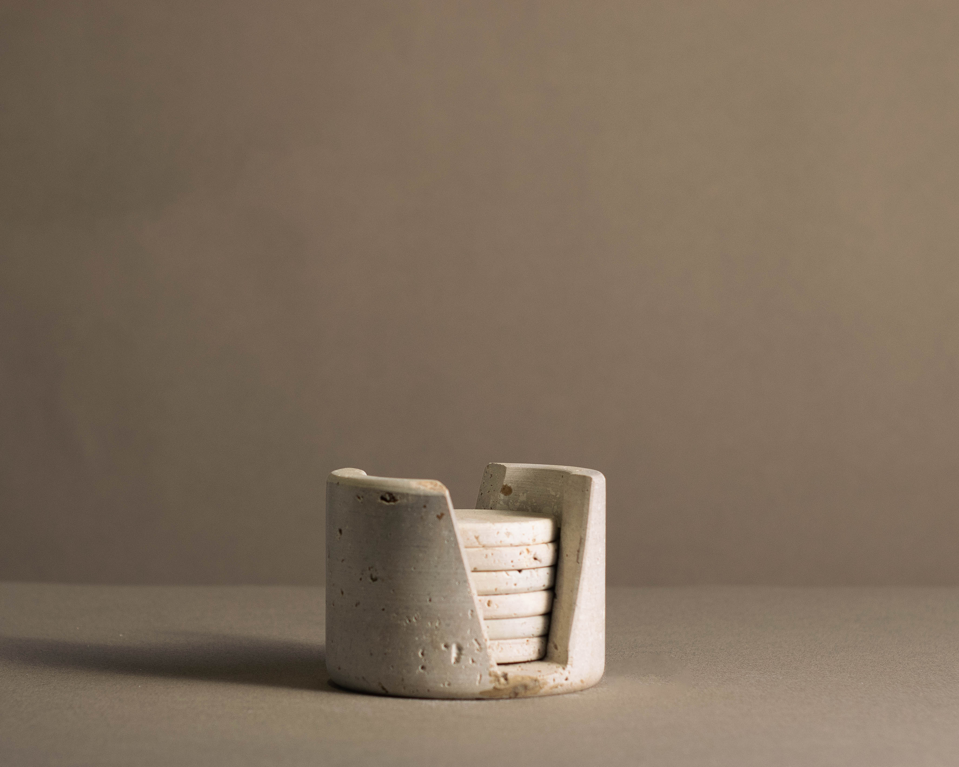 Murmor coasters with holder in travertine elegantly displayed on a dining table.